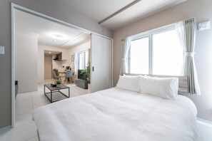 A modern hotel room with a large bed, a small table, a desk, and a view of the outside through a window. - NEXUS (Sapporo)