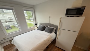 Une chambre à coucher comprenant un lit, une table de chevet, une lampe, un four à micro-ondes et un réfrigérateur.
