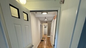 Un couloir étroit avec une porte sur la gauche, un luminaire au-dessus et un paillasson à l’entrée.