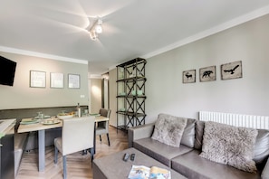 A modern living room with a sofa, a coffee table, a dining area with a table and chairs, and wall art. - Boutique Apartment Limone Ski In Ski Out (Limone Piemonte)