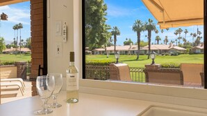 A table with two wine glasses and a bottle of wine, a window with a view of a golf course, and a brick pillar.