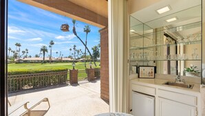 A patio with a view of a golf course, a bar area with glassware, and a stone bench.