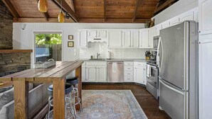 A modern kitchen with white cabinets, stainless steel appliances, and a wooden ceiling.