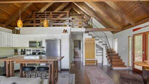 A spacious loft-style living area with a kitchen, wooden beams, a staircase, and a cozy seating area.