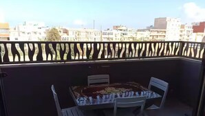 Ein Balkon mit Tisch und Stühlen, Blick auf die Stadtlandschaft und einem dekorativen Geländer.