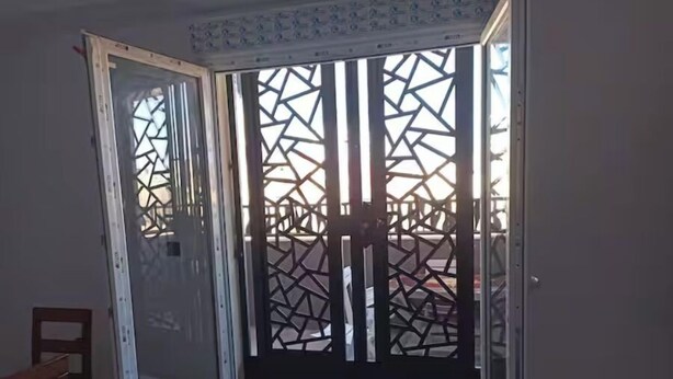 Ein Zimmer mit einer Schiebeglastür, die zu einem Außenbereich mit einem geometrisch gemusterten Sichtschutz führt.