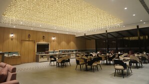 Un comedor amplio con múltiples mesas y sillas, un panel de pared de madera y un techo decorado con numerosas luces.