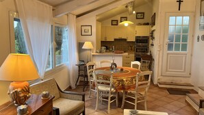 A cozy dining area with a round table, chairs, and a lamp. A kitchen is visible in the background with cabinets and appliances. - Sète - La Vigie Singulière (Sète)