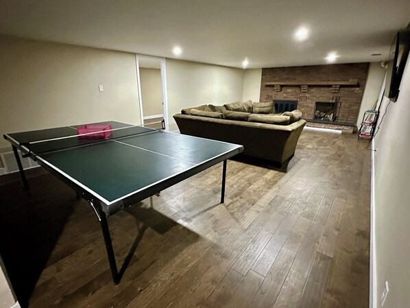 Una sala de estar con mesa de ping pong, sofá y chimenea.
