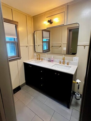 A bathroom with a double vanity, a large mirror, and a window with blinds.