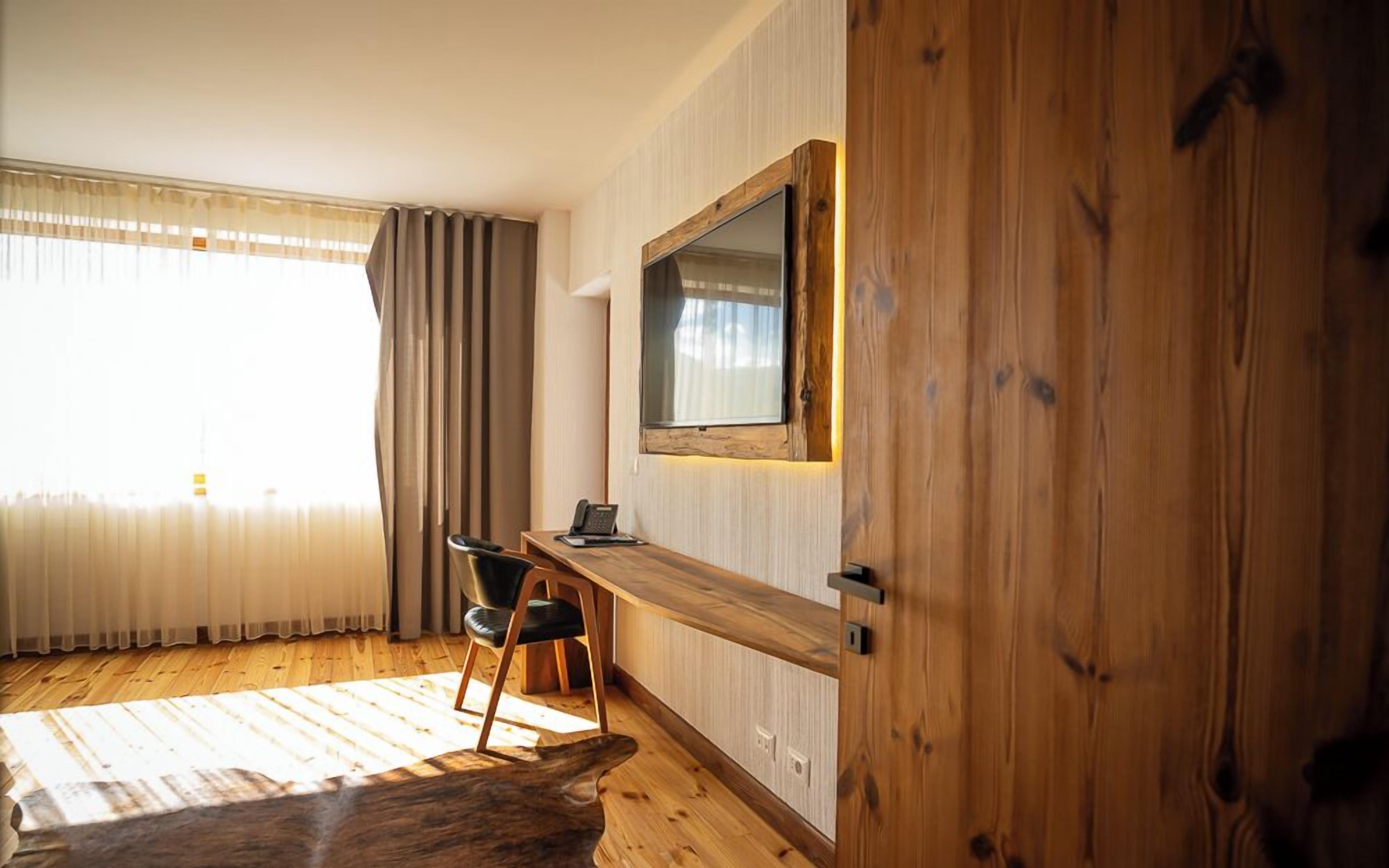 Una habitación con un escritorio de madera, una silla, un espejo grande y un ventanal con cortinas.