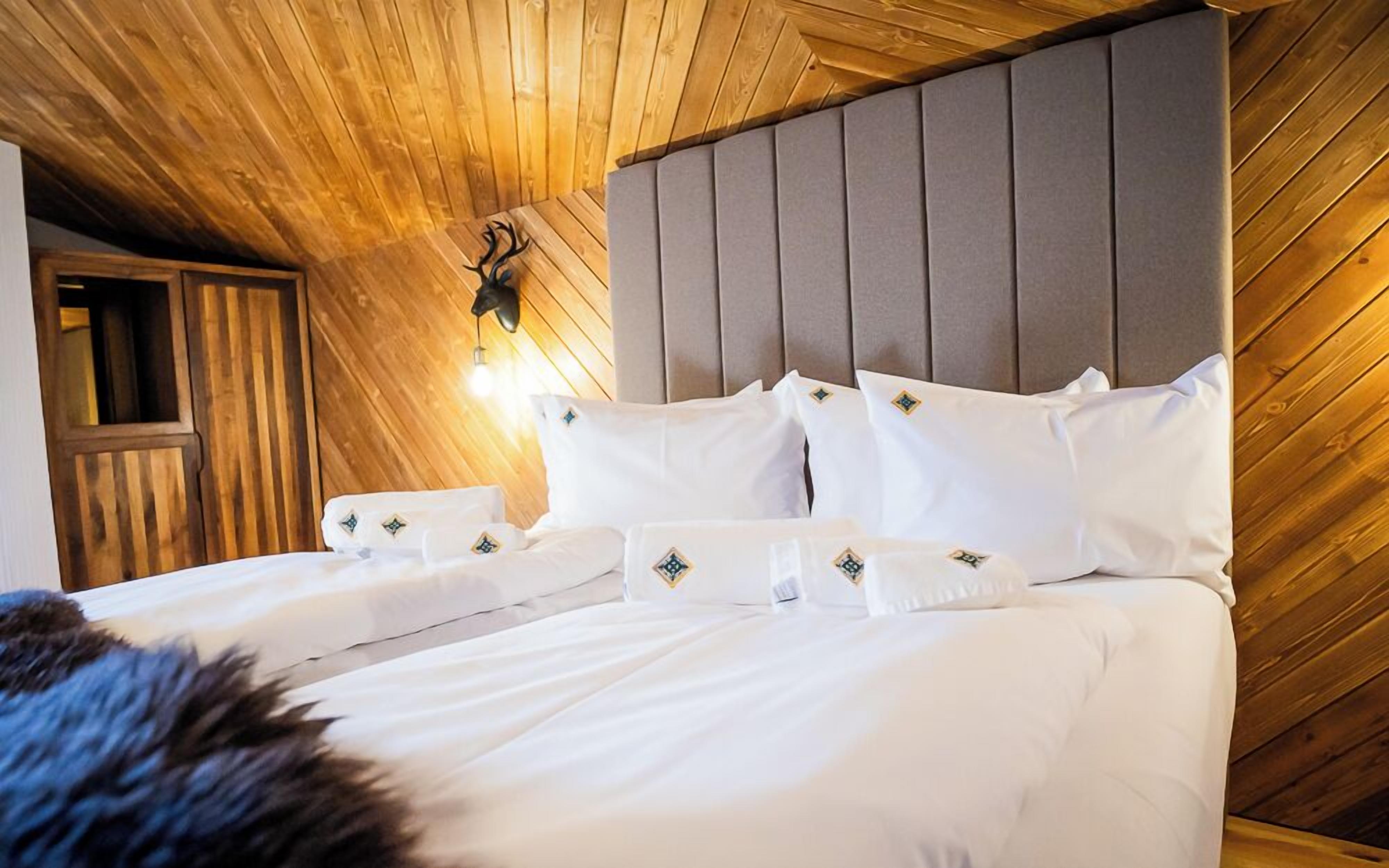 A bedroom with a wooden ceiling, a grey headboard, and white bedding with decorative pillows.