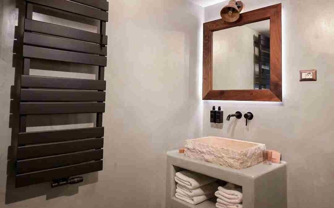 A bathroom with a wooden slatted towel rack, a mirror with a wooden frame, and a sink with stacked towels.