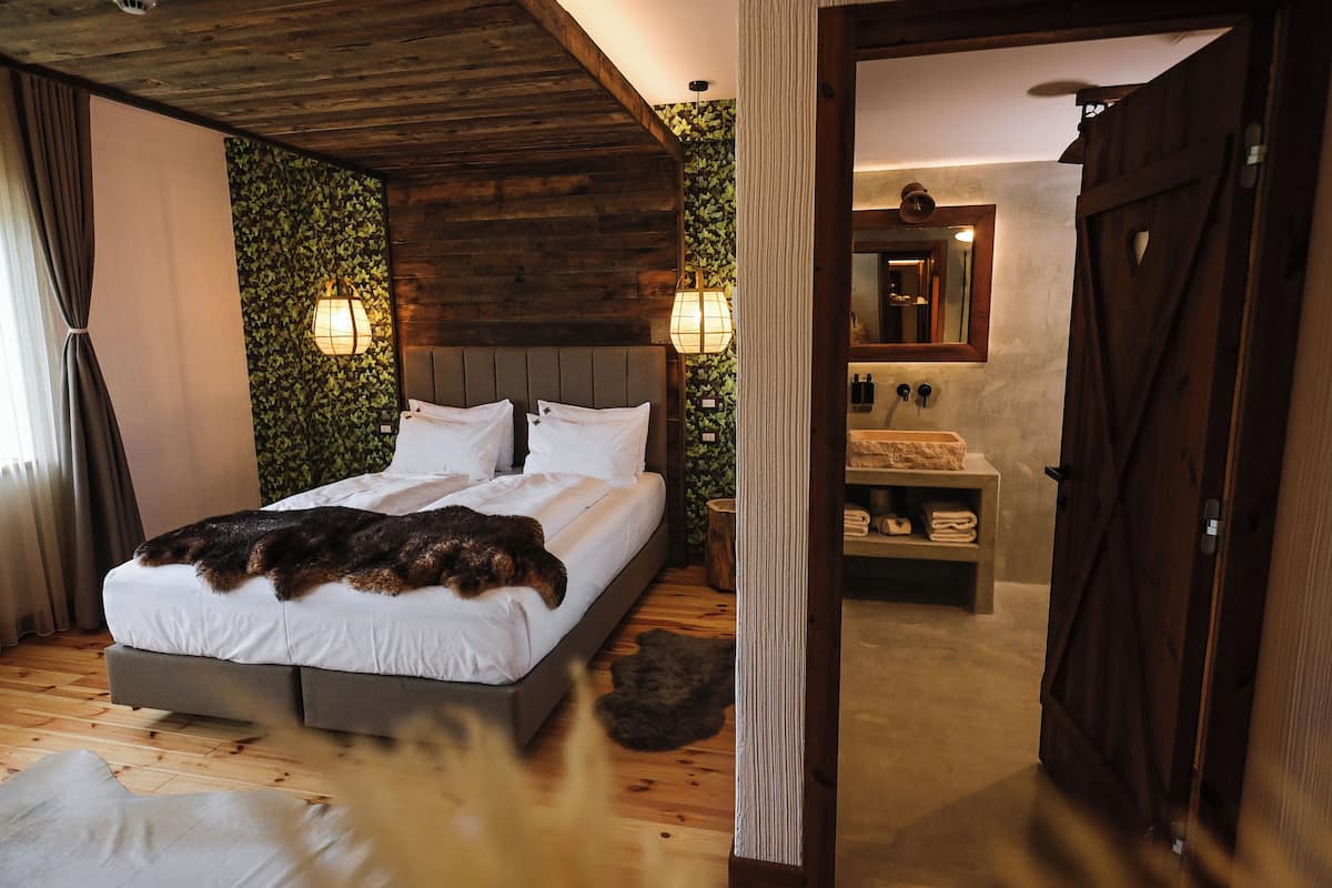 Une chambre avec un plafond en bois, un lit recouvert de draps blancs, deux lampes fixées au mur et un banc en bois sur lequel sont posées des serviettes.