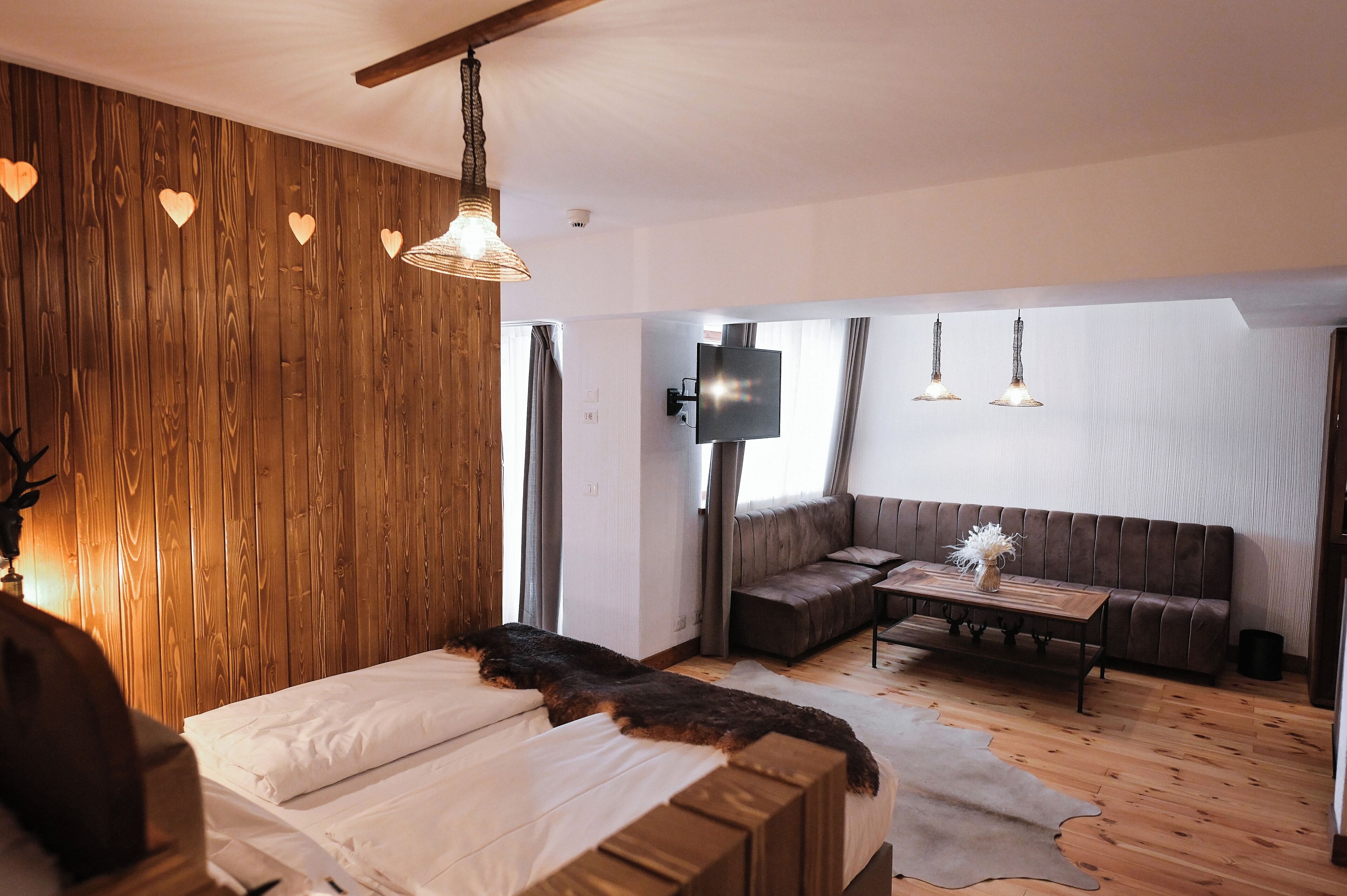 Un dormitorio con pared de madera, una cama, un banco, un sofá, un televisor y suelo de madera.