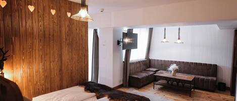 Un dormitorio con pared de madera, una cama, un banco, un sofá, un televisor y suelo de madera.