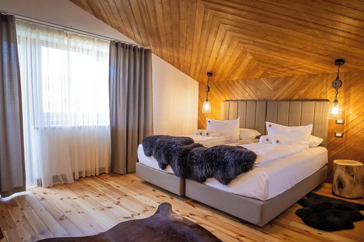 Une chambre à coucher avec un plafond en bois, un lit recouvert de draps blancs, deux lampes de chevet et une fenêtre avec des rideaux.