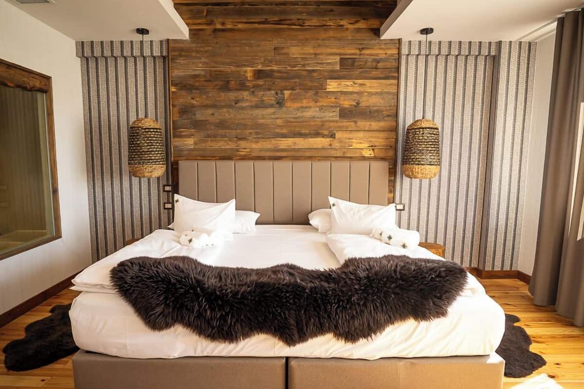 Un grand lit recouvert d’une couverture moelleuse, un lambris en bois sur le mur et un miroir sur le côté gauche.