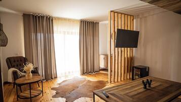 A modern living room with a wooden floor, a round coffee table, a leather sofa, and a TV mounted on a wooden panel.
