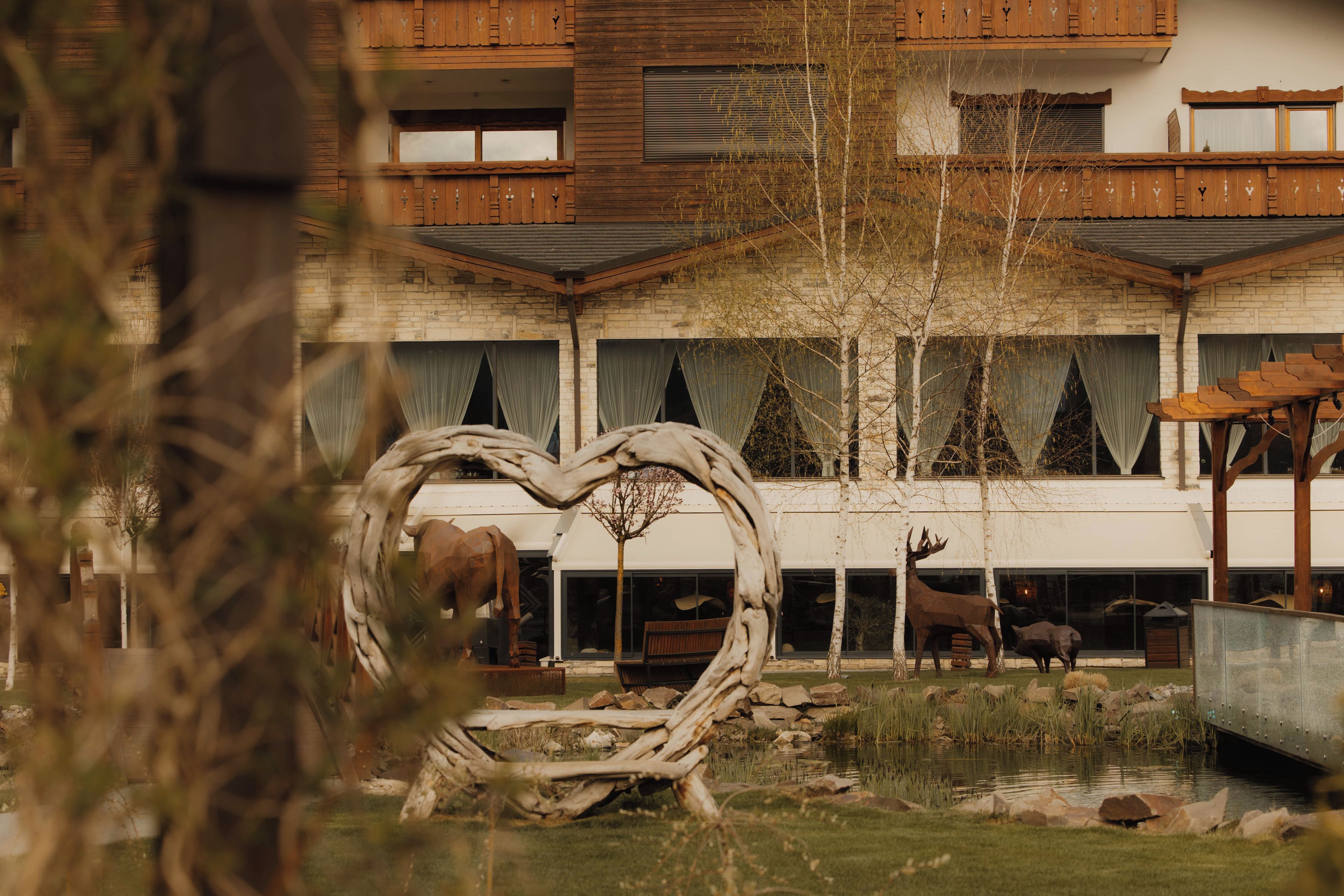 Un edificio con fachada de madera, varias ventanas y un patio con una escultura en forma de corazón y esculturas de animales.