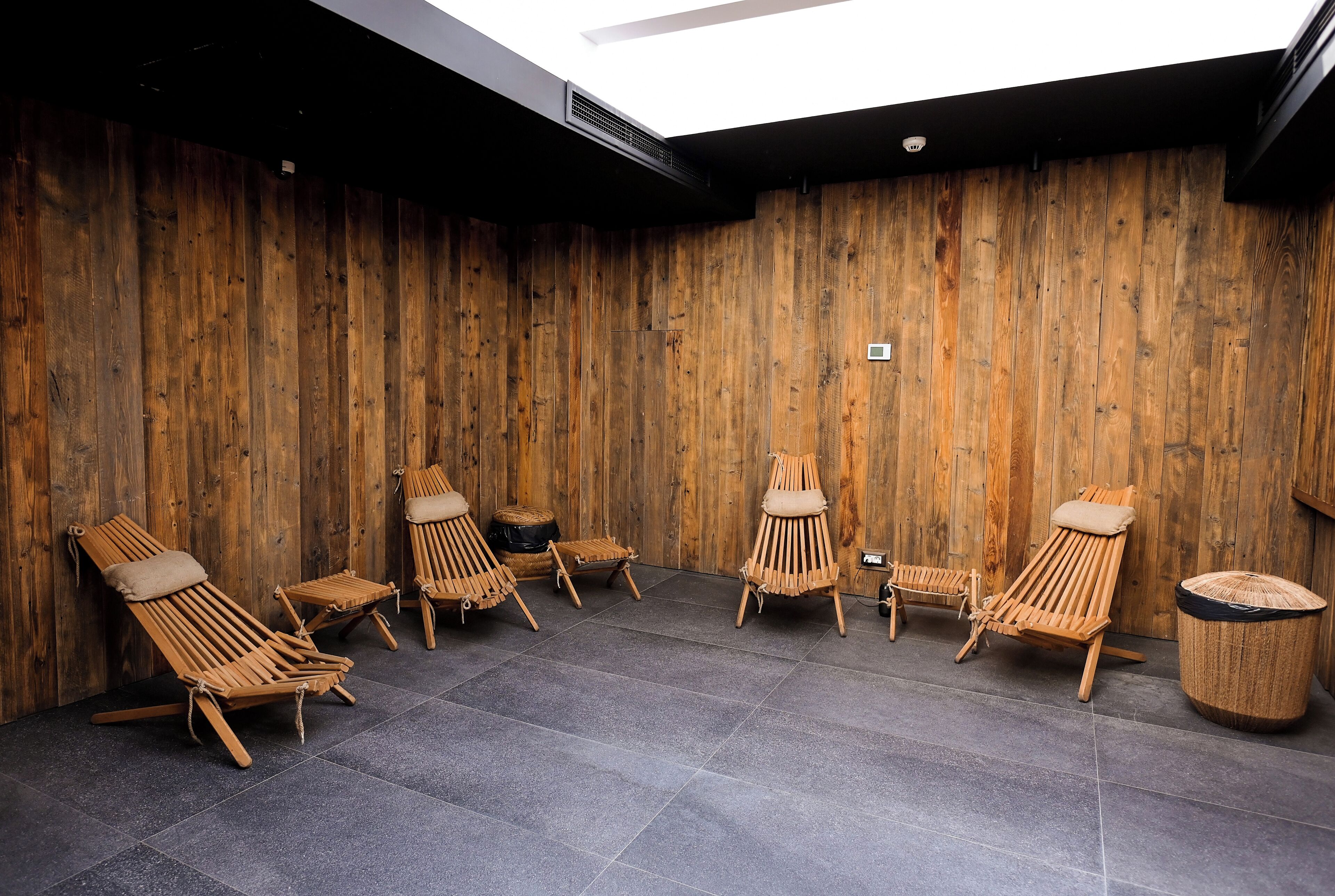 Eine Holzwand mit Deckenventilator, gefliestem Boden und mehreren Holzliegestühlen.