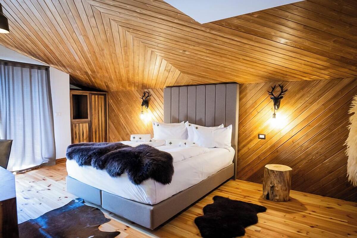 Une chambre avec un plafond en pente, un lit avec une literie blanche, deux lampes fixées au mur et une décoration représentant une tête de cerf.