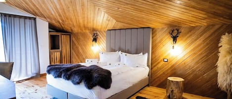 A bedroom with a sloped ceiling, a bed with white bedding, two wall-mounted lights, and a deer head decoration.