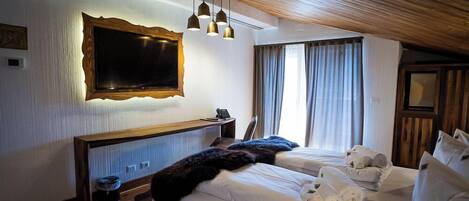 A hotel room with a large bed, bedside tables, a desk, a chair, a TV, and a window with curtains.