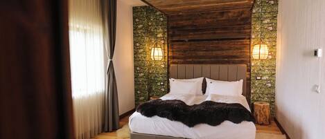 A bedroom with a wooden ceiling, a bed with white bedding, two wall-mounted lights, and a rustic wooden floor.