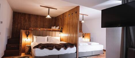 A modern bedroom with a wooden accent wall, two beds, a large flat-screen TV, and a staircase.