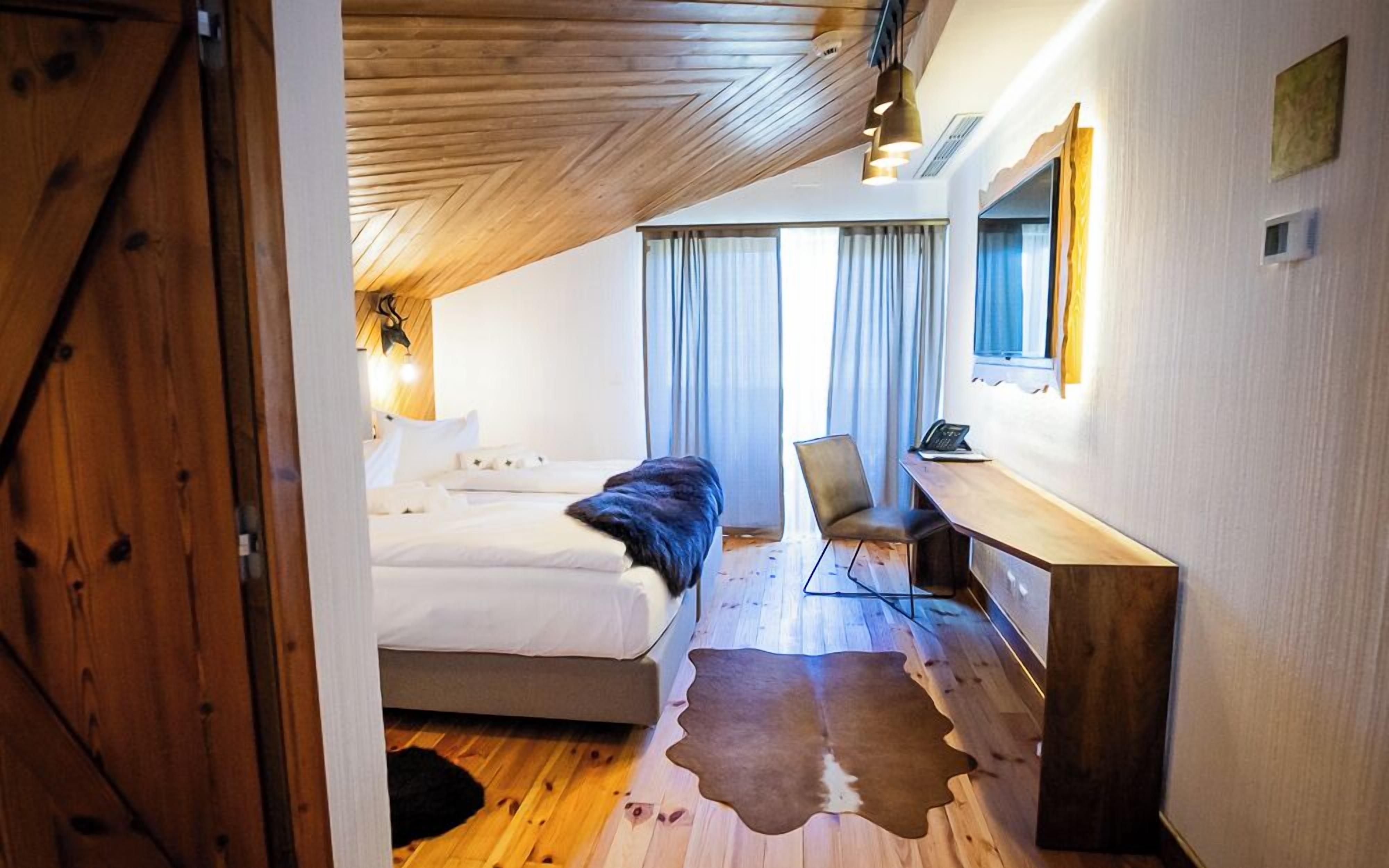 A modern hotel room with a wooden ceiling, a bed, a desk, and a chair.