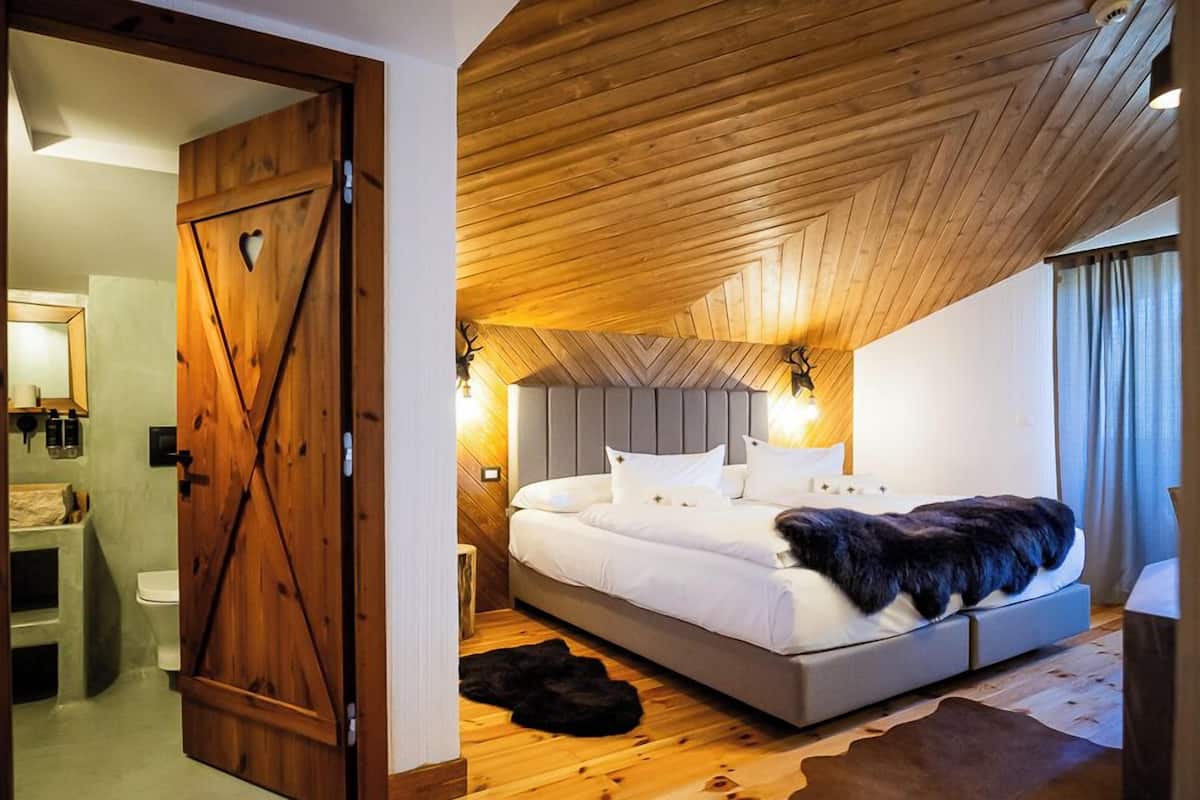 Une chambre avec un plafond en bois, un lit avec une literie blanche et un plaid en fausse fourrure noire.