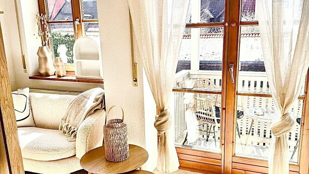 Una habitación acogedora con sofá, una pequeña mesa redonda y vistas a un paisaje urbano a través de amplias ventanas.