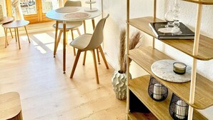 Una habitación bien iluminada con comedor, televisor montado en la pared y una estantería con adornos.