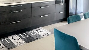A modern kitchen with dark cabinets, a white countertop, and a dining area with teal chairs.