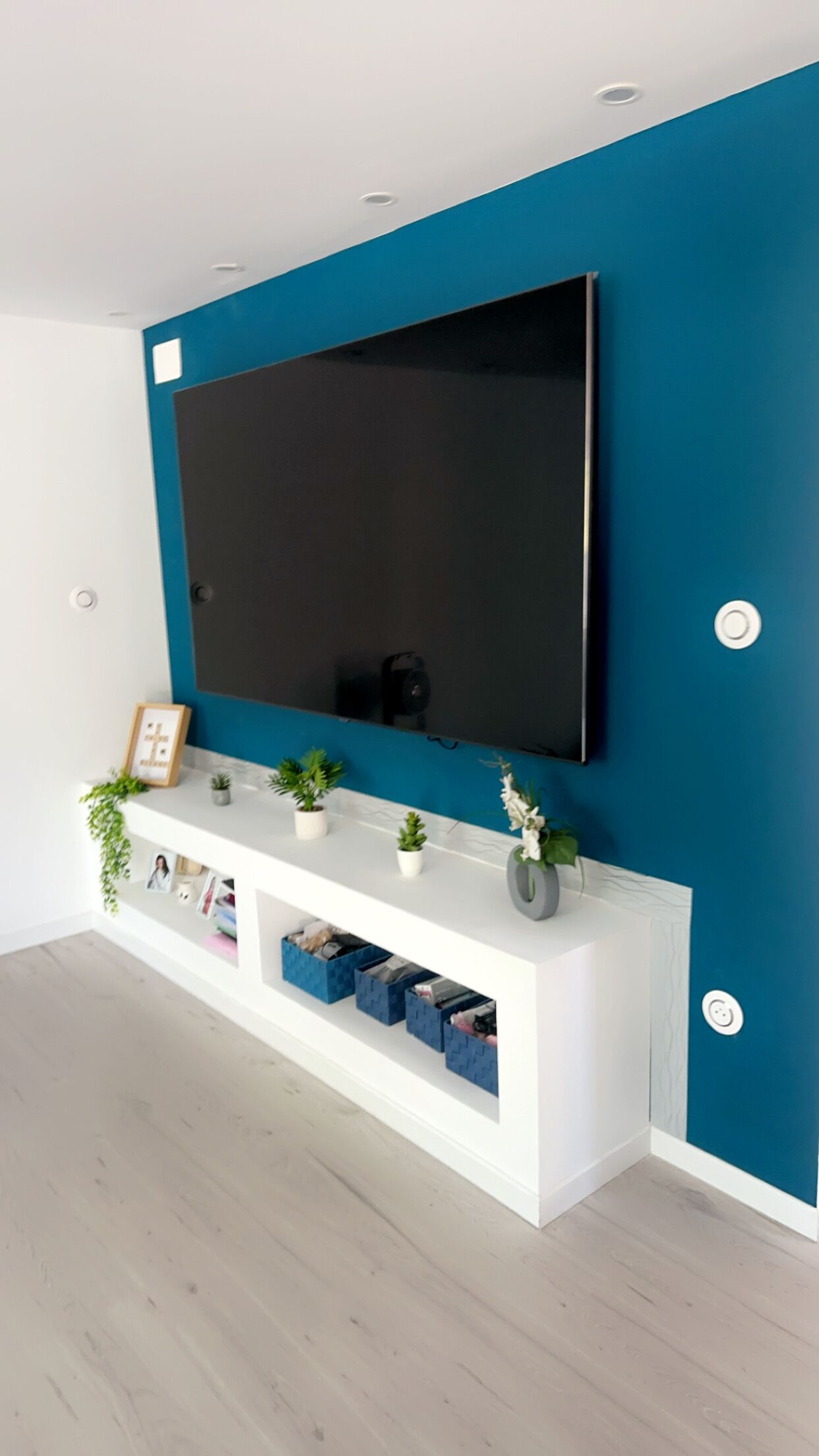 Un soggiorno moderno con un'ampia televisione a schermo piatto montata su una console bianca, con una parete verde acqua.
