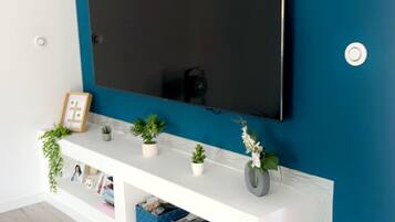 Un soggiorno moderno con un'ampia televisione a schermo piatto montata su una console bianca, con una parete verde acqua.