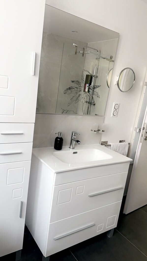 A modern bathroom with a white vanity, a large mirror, a glass shower enclosure, and a white sink.
