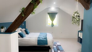 A bedroom with a sloped ceiling, a bed with blue and white bedding, a small window with curtains, and a hanging plant.