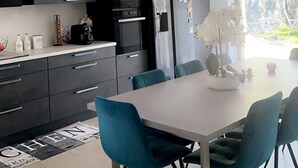 A modern kitchen with dark cabinets, a stainless steel refrigerator, and a dining area with teal chairs and a white table.