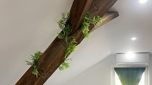 A bedroom with a sloped ceiling, a bed with white and blue bedding, a window with a curtain, and a plant on the ceiling.