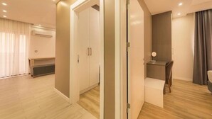A modern hotel room with a wooden floor, a desk with a chair, a wardrobe, and a bed.