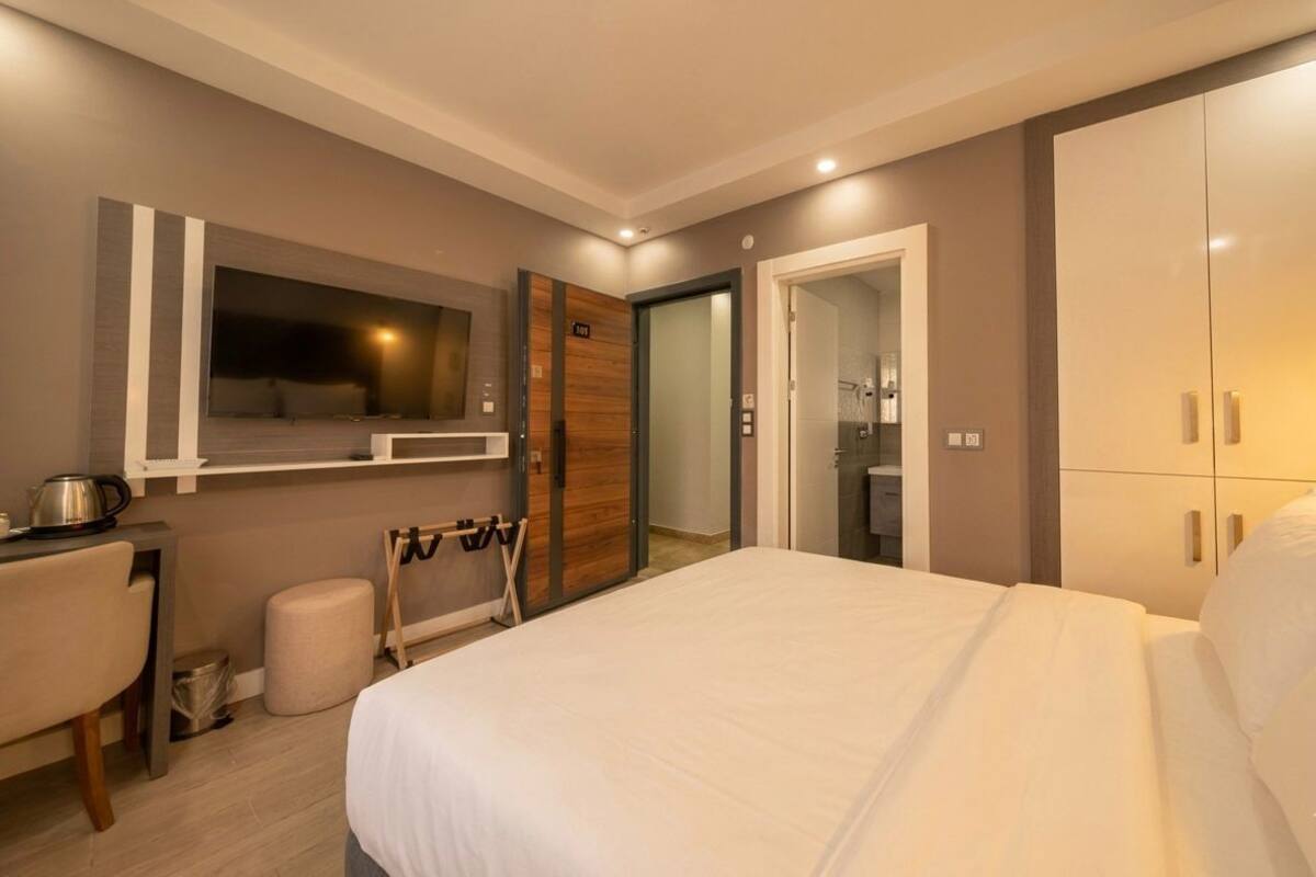 A modern hotel room with a large bed, a desk, a mirror, and a wardrobe.