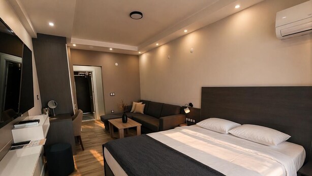 A modern hotel room with a large bed, a sofa, a desk with a chair, a small table, and a mirror.