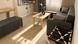 A modern living room with a sofa, a coffee table, a TV mounted on the wall, and a window with curtains.