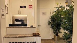 A reception desk labeled 'RESEPSİYON' with a printer, a sign indicating room number 112, and a potted plant in the hallway.