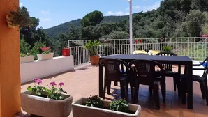 A terrace with a table and chairs, potted plants, and a view of a hilly landscape. - Vila with private pool, sea view 7km away Pets welcome (Calonge)
