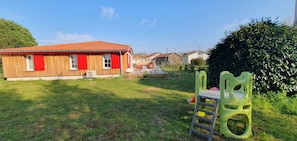 A wooden house with red shutters, a grassy yard, and a green plastic play structure.