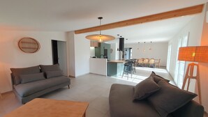 A modern living room with a sofa, a wooden coffee table, and a dining area with chairs and a table. - Sunny vacation home. Ideally located between lake, beach and forest. (Sanguinet)