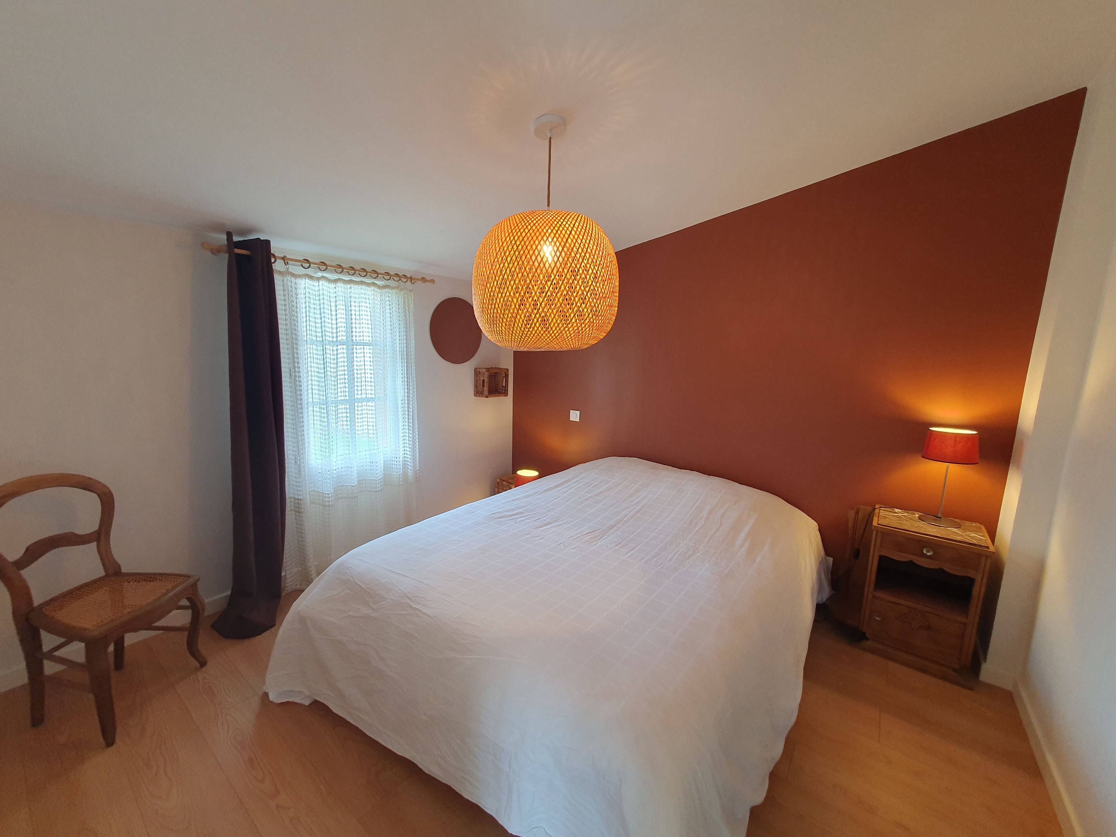 Quarto com cama, uma cadeira, mesa de cabeceira com abajur e luminária pendente.